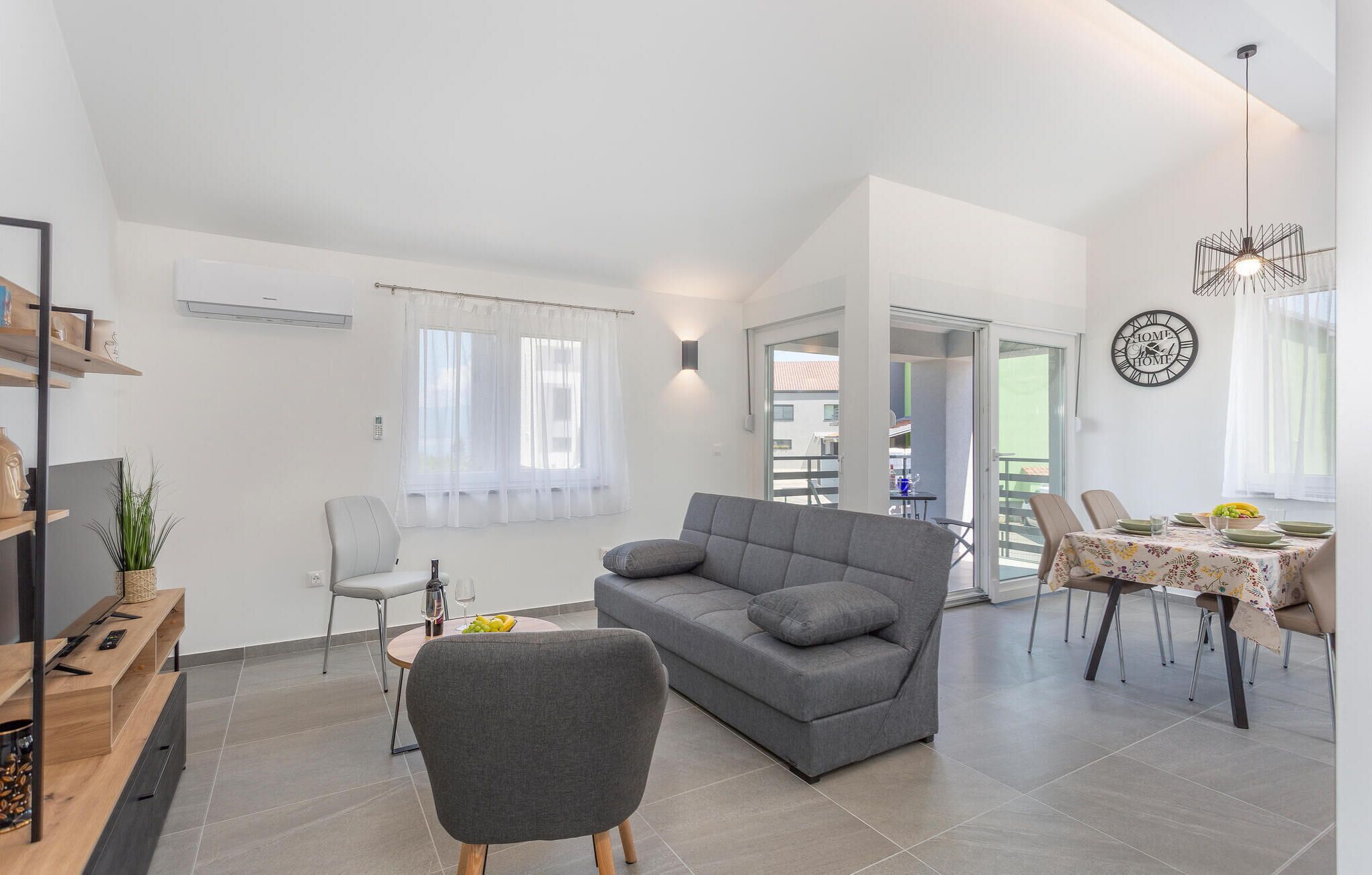 Ein modernes Wohnzimmer mit grauem Sofa, einem Essbereich mit Tisch für zwei Personen und einem Balkon mit Blick.