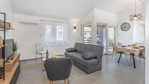 En moderne stue med en grå sofa, et spiseområde med et bord dækket til to, og en balkon med udsigt.