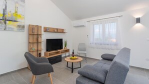 En moderne stue med et fladskærms-tv, en grå sofa og et lille træbord med en skål frugt.