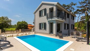 En toetages bygning med swimmingpool, udendørs siddepladser og en balkon.