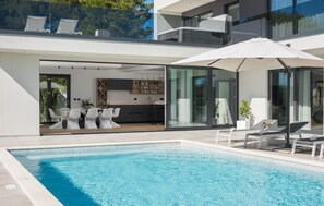 A modern house with a swimming pool, outdoor seating, and a kitchen visible through glass doors. - Lovely home in Medulin (Medulin)