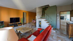 A living room with a red sofa, a TV, and a coffee table. There is a staircase leading to a kitchen with a clock on the wall. - Cozy home in Lançon-Provence (Lançon-Provence)