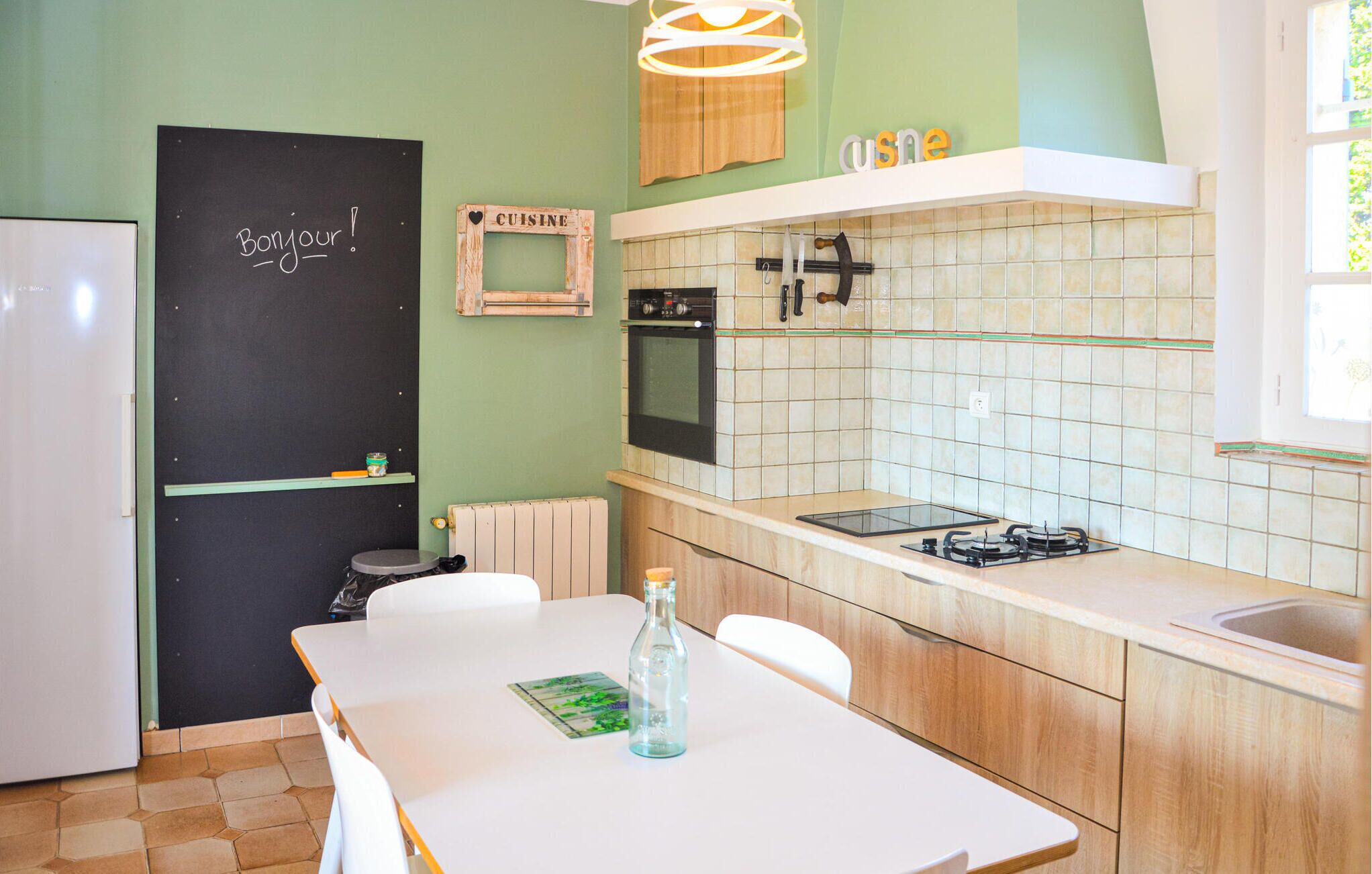 Una cocina con una mesa blanca, una botella y un letrero en la puerta que dice 'Bonjour!'.