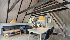 Ett mysigt vardagsrum i loftstil med en matplats, synliga träbjälkar och utsikt över omgivningen.