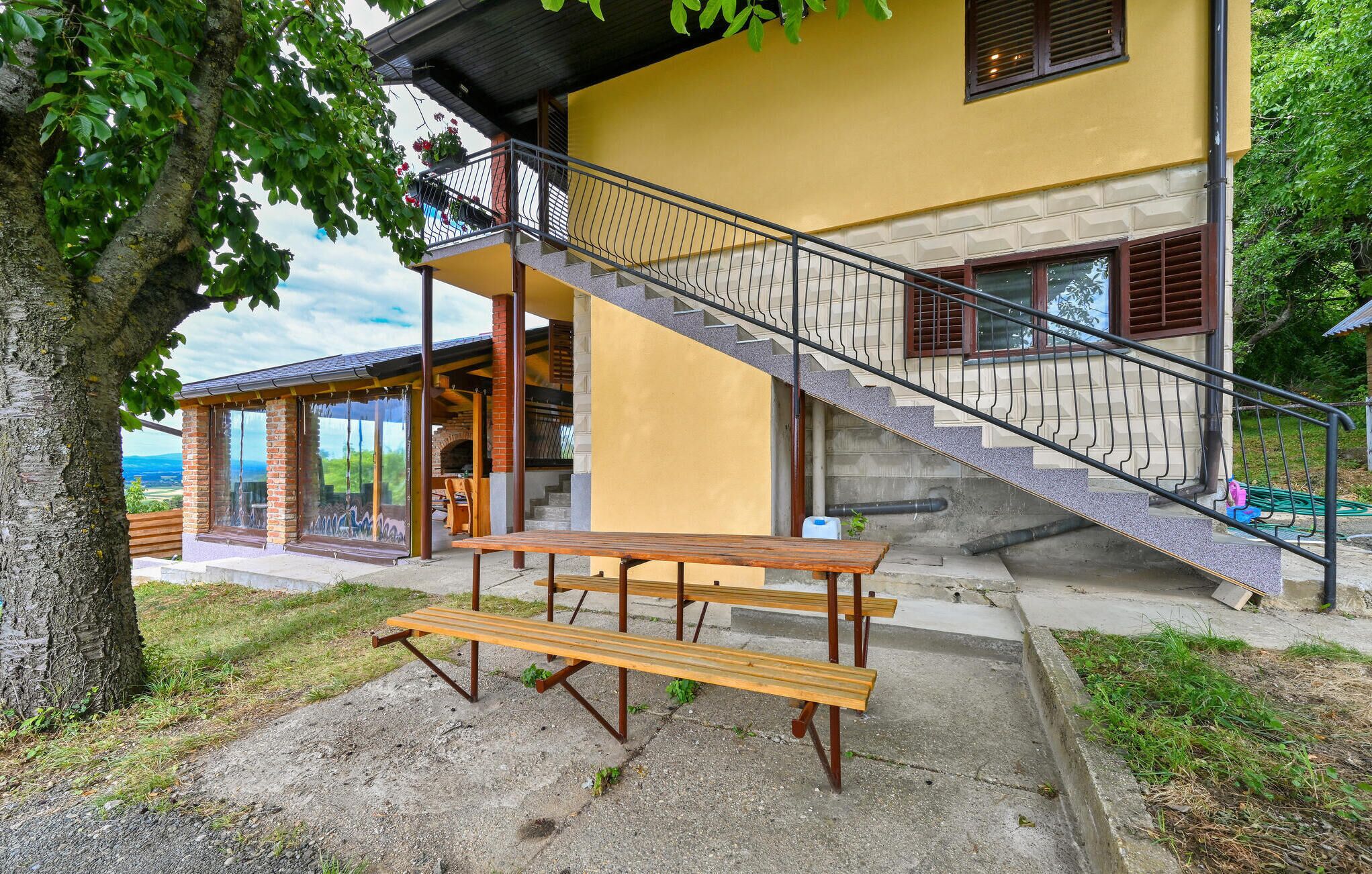 Ein gelbes Gebäude mit einer Treppe, die zu einem Balkon führt, einer hölzernen Bank und Blick auf die Landschaft.