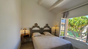 Un dormitorio con una cama, dos mesitas de noche, un ventanal con vistas a zonas verdes y un techo con vigas a la vista.