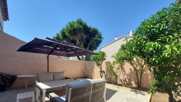 Un patio al aire libre con una mesa y sillas, una pequeña mesa blanca y una pérgola que proporciona sombra.