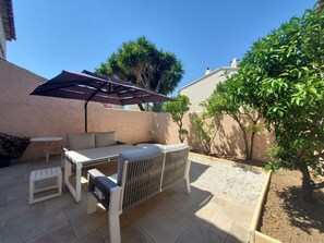 Een terras met een tafel, stoelen, een kleine witte tafel en een pergola voor beschutting.