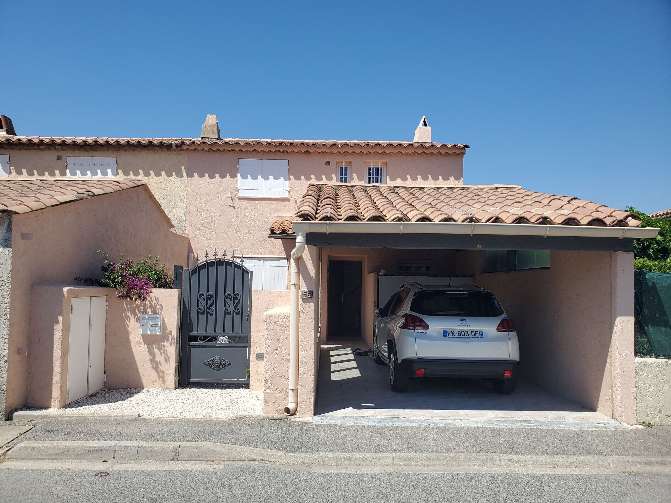 A residential building with a covered garage, a gated entrance, and a parked car.