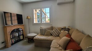 Una sala de estar con un sofá, televisor, estantería y ventana con vista a edificios.