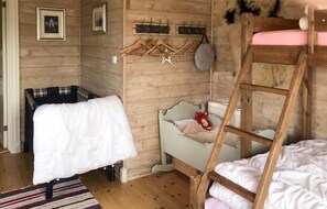 A wooden room with bunk beds, a small desk, and a hanging coat rack.