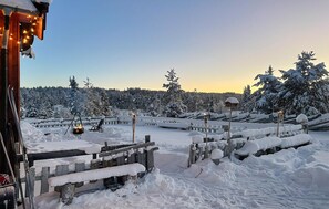 A snow-covered outdoor area with wooden fences, a fire pit, and a bench.
