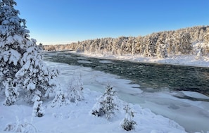 Ein Fluss, umgeben von schneebedeckten Bäumen und wolkenlosem Himmel.