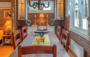 Un interior de madera con una mesa de comedor, sillas, una araña y un ventanal con cortinas.