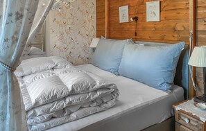 Una cama bien hecha con ropa de cama blanca y azul claro, cabecera de madera y una pared con estampado floral.