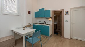 Eine kompakte Küche mit türkisfarbenen Schränken, einer weißen Arbeitsplatte und einem blauen Stuhl.