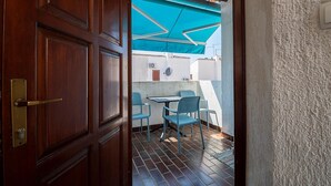 Eine Holztür führt zu einem Balkon mit blauem Sonnensegel, einem Tisch und zwei Stühlen.