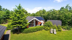 A house with a solar panel roof, surrounded by lush greenery and a well-maintained lawn.