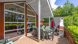 A covered patio with outdoor furniture, a barbecue grill, and a view of the surrounding greenery.