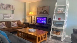 En stue med en brun sofa, et træ sofabord, et fjernsyn med lilla lys, en lampe og en hvid reol med et 'Welcome'-skilt.