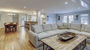 A spacious living room with a large sectional sofa, wooden coffee table, and a dining area with a wooden table and chairs.