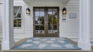 A front porch with a blue mat featuring a turtle pattern, a double door with glass panels, and two wall-mounted lanterns.