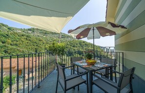 Un balcon avec une table dressée pour deux personnes, une chaise et un pot de fleurs.