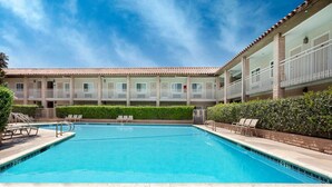 A swimming pool with lounge chairs, a building with balconies, and a clear sky. - Travelodge by Wyndham Orange County Airport/ Costa Mesa (Costa Mesa)