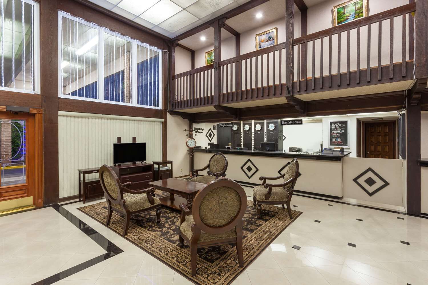 A lobby with a reception desk, a television, a dining area with a table and chairs, and a staircase leading to an upper level.