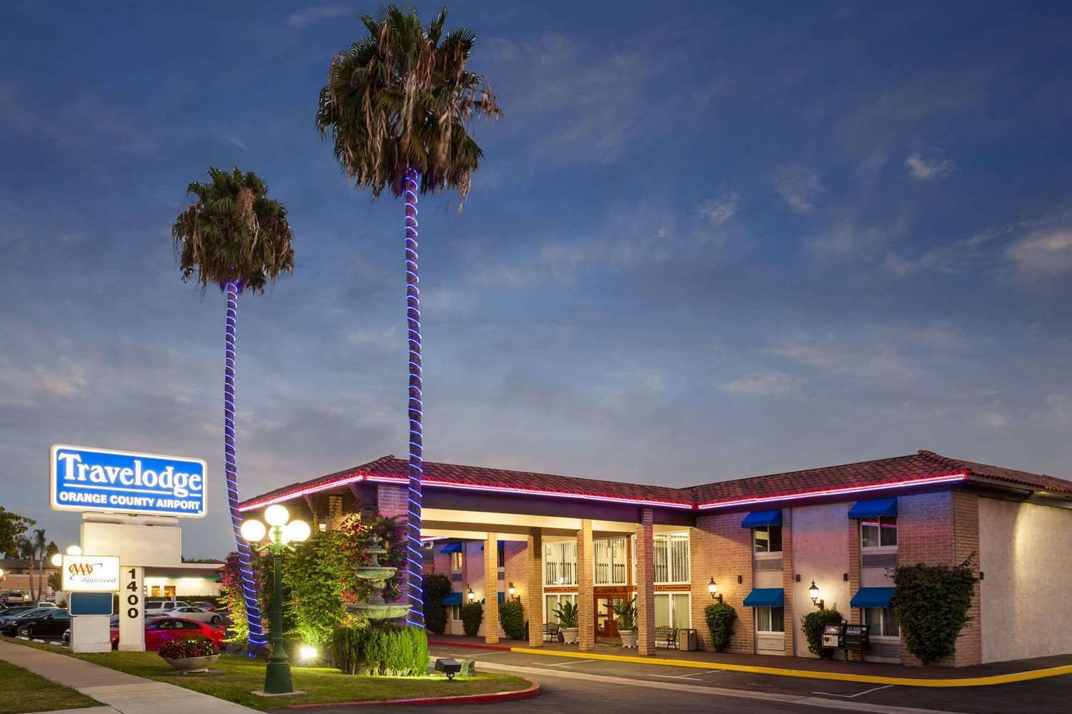 A Travelodge Orange County Airport hotel with a brick facade, palm trees, and a well-lit entrance.