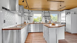 Una cocina moderna con armarios blancos, techo de madera y un ventanal con vistas a la vegetación.