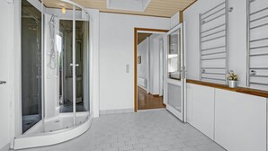 Un baño moderno con ducha de vidrio, piso de baldosas blancas y tocador de madera con lavamanos.