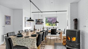 Un comedor con una mesa larga dispuesta para una comida, un ventanal con vistas a árboles y un estufa de leña.