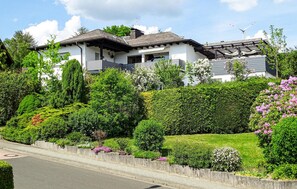 Stunning two-story residence with a traditional pitched roof and balcony, surrounded by beautifully maintained gardens and a wind turbine in the background.