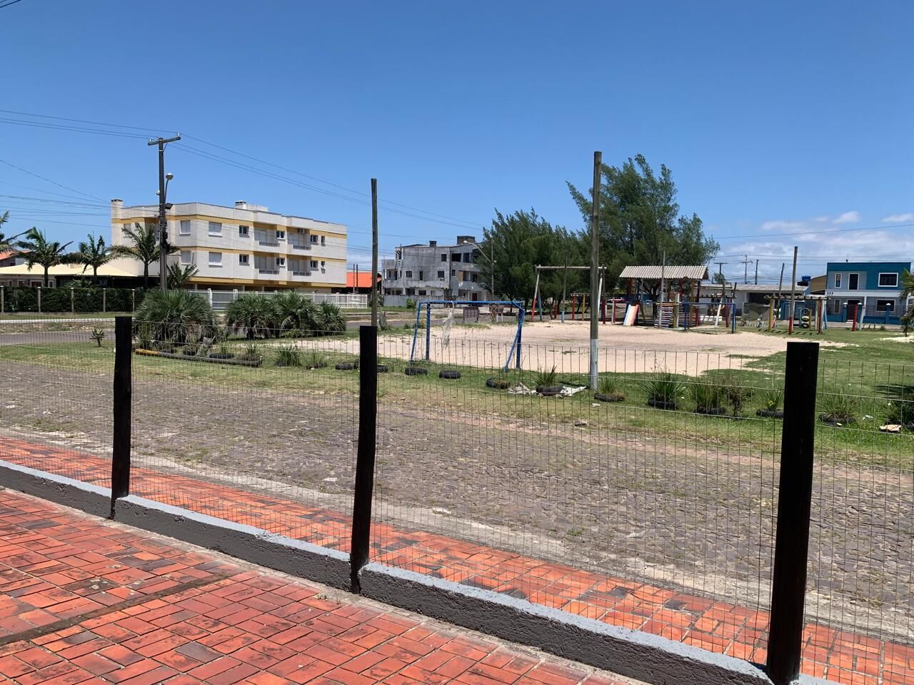 A paved area with a fence, a building in the background, and a clear sky.