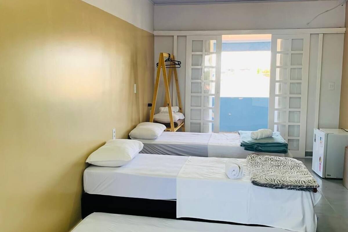 Hotellihuone, jossa on kolme sänkyä, puinen riipputuoli, pieni jääkaappi ja näkymä merelle.