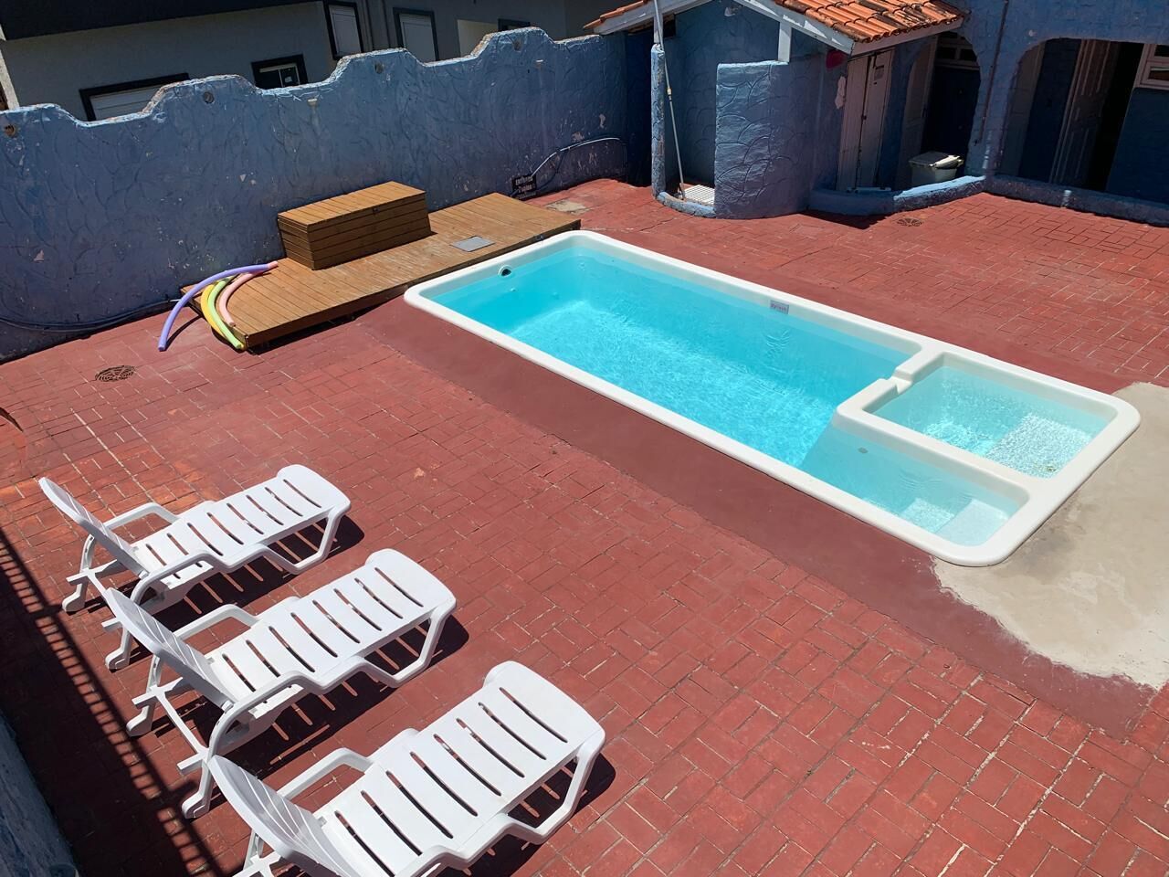A rooftop swimming pool with a wooden deck and white lounge chairs.
