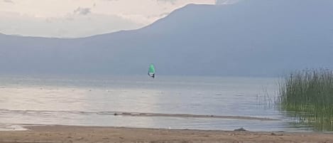 Un lago tranquilo con un kitesurfista a lo lejos, rodeado de montañas y un cielo despejado.