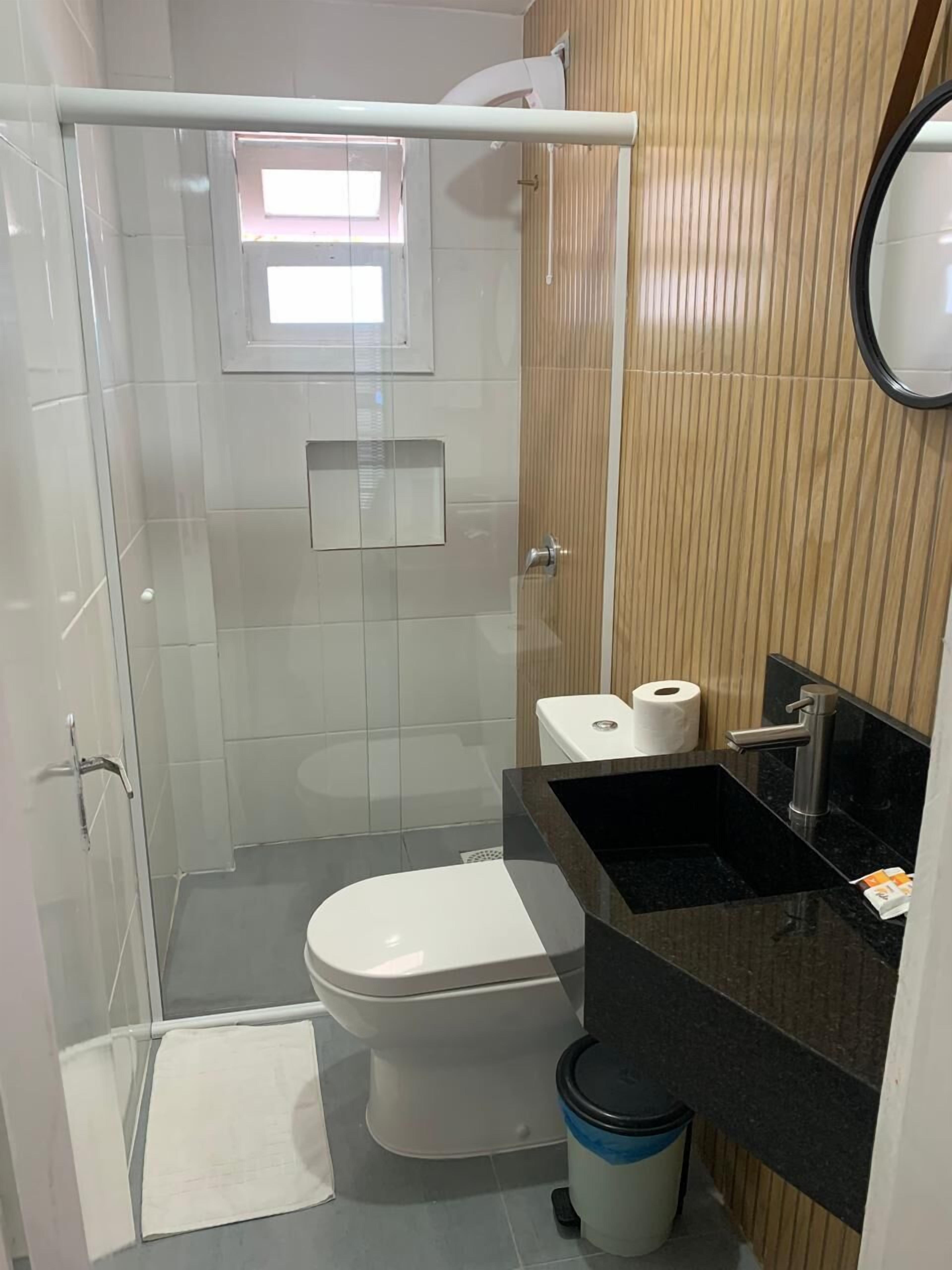 A modern bathroom with a glass-enclosed shower, a toilet, a sink with a black countertop, and a wooden panel wall.