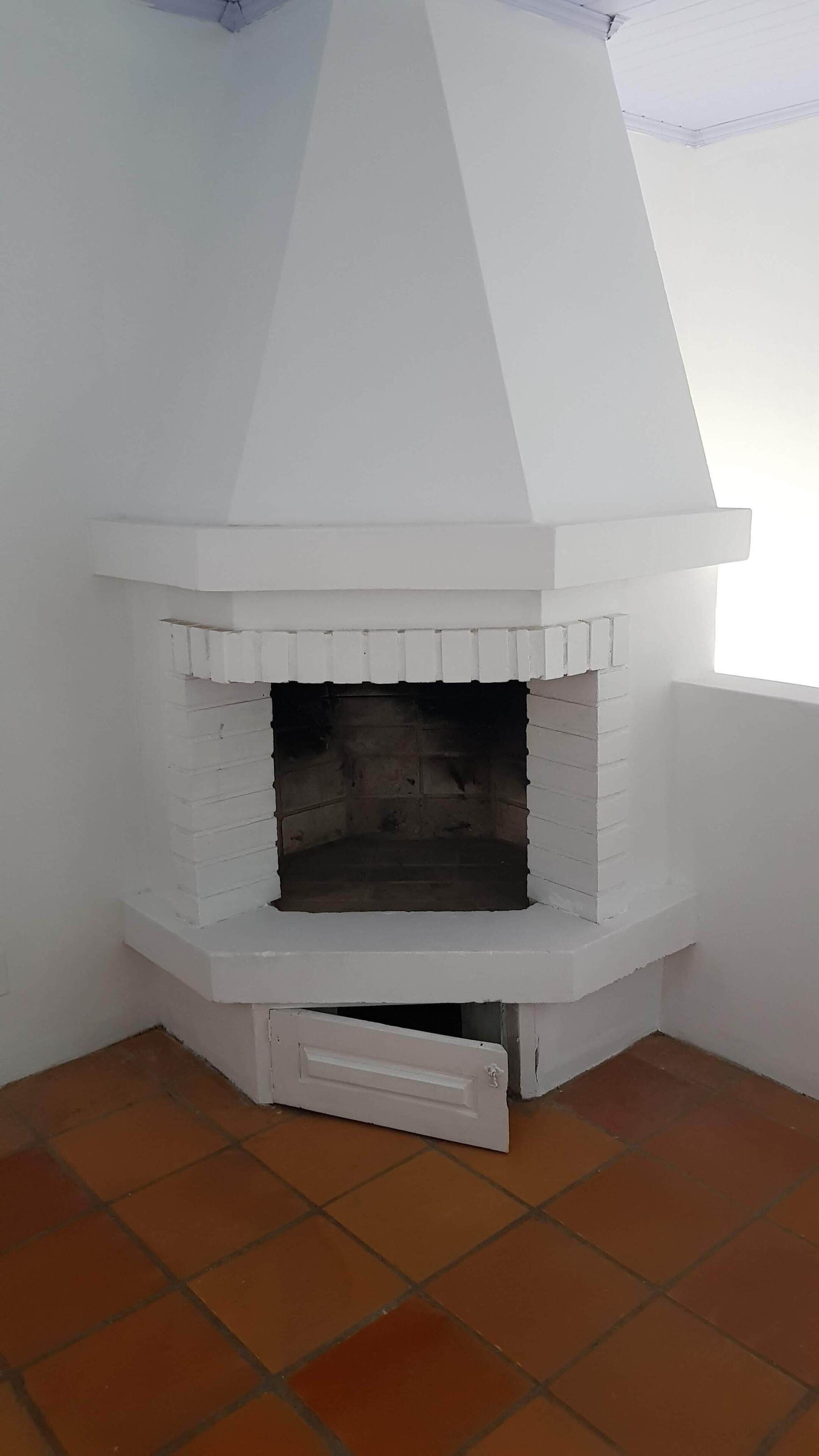 Ein weißer Kamin mit Ziegelbasis, platziert in einer Ecke eines Raumes mit Terrakottafliesen.