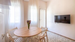 A room with a round wooden table, white chairs, a vase with flowers, a flat-screen TV mounted on the wall, and a patterned floor. - Beautiful apartment in San Javier (San Javier)