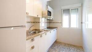 A compact kitchen with white cabinets, a granite countertop, a microwave, and a window with blinds. - Beautiful apartment in San Javier (San Javier)