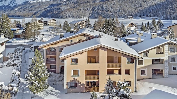 Ein schneebedecktes Gebäude mit mehreren Balkonen, umgeben von schneebedeckten Bäumen und Bergen im Hintergrund.