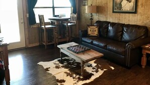 L’intérieur d’un chalet rustique, avec un canapé en cuir, une table basse en bois et un tapis en peau de vache.