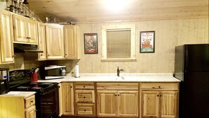 Une cuisine avec des meubles de rangement en bois, un réfrigérateur noir, un four à micro-ondes et une cuisinière. Deux tableaux encadrés sont accrochés au mur.