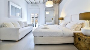 A modern, white-themed bedroom with a large bed, a sofa, and a bedside table with a lamp. - Amazing villa (Άγιος Ιωάννης Διακοφτης)