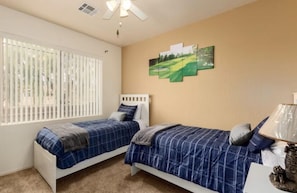 A bedroom with two single beds, a ceiling fan, a window with blinds, and a wall-mounted painting. - Scottsdale Condo Centrally Located with Heated Pool, Game Room and Gym (Scottsdale)