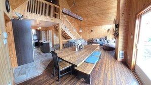 A wooden cabin interior with a large dining table, benches, a staircase, and a cozy seating area. - Waterfront Family Cottage! (Notre-Dame-de-Pontmain)