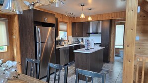 A modern kitchen with wooden paneling, stainless steel appliances, and pendant lighting. - Waterfront Family Cottage! (Notre-Dame-de-Pontmain)