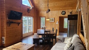 A wooden cabin interior with a dining area, a sofa, a TV, and a mounted deer head. - Waterfront Family Cottage! (Notre-Dame-de-Pontmain)